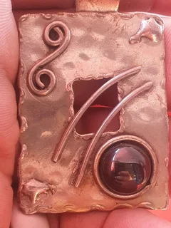 metal pendant with a hammered texture, swirl design, and a amber stone