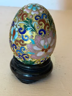 A vintage small Chinese hand-painted cloisonné egg with floral motifs on a wooden stand.
